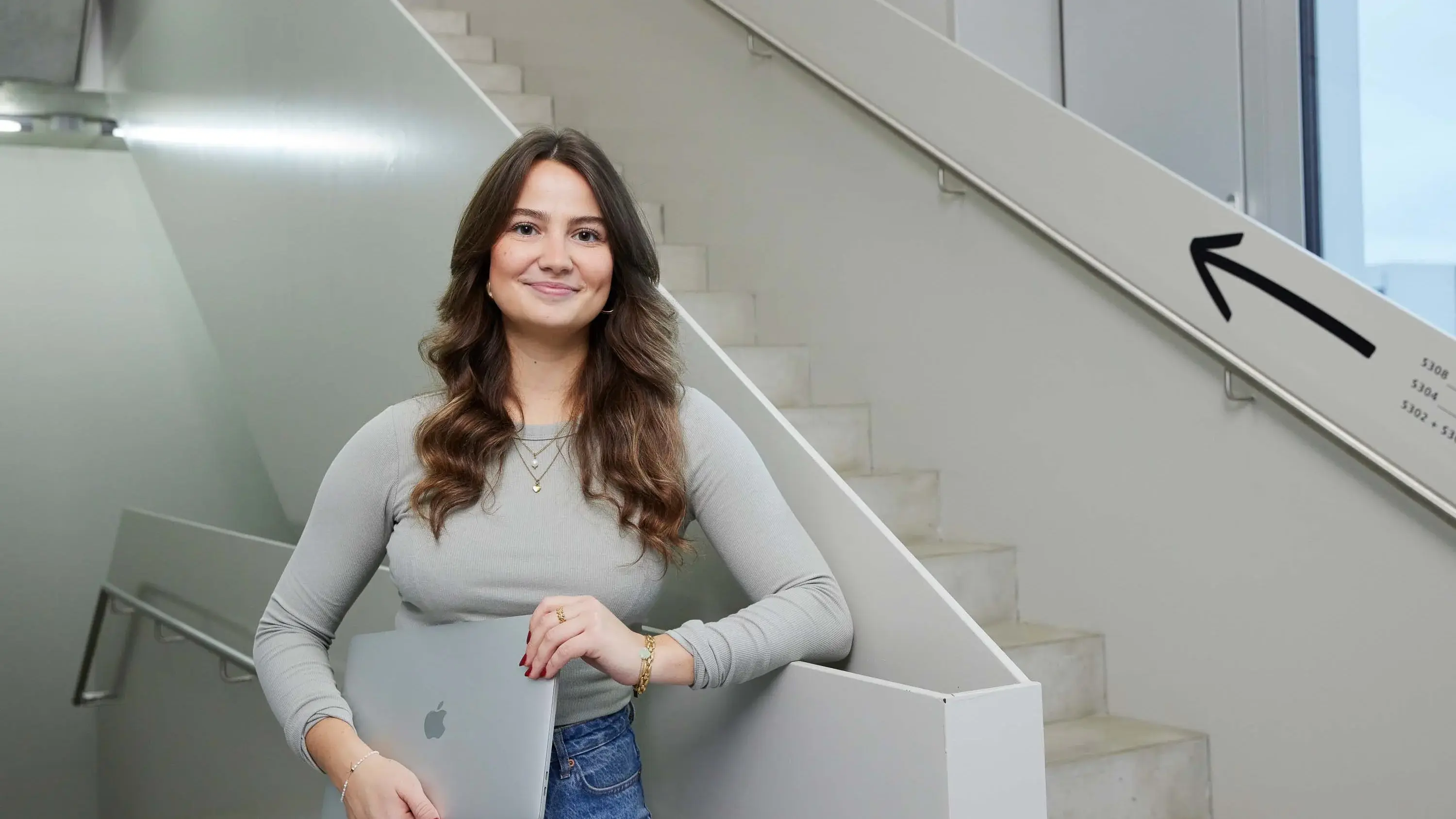 Eine Studierende posiert mit ihrem Laptop an einer Treppe.
