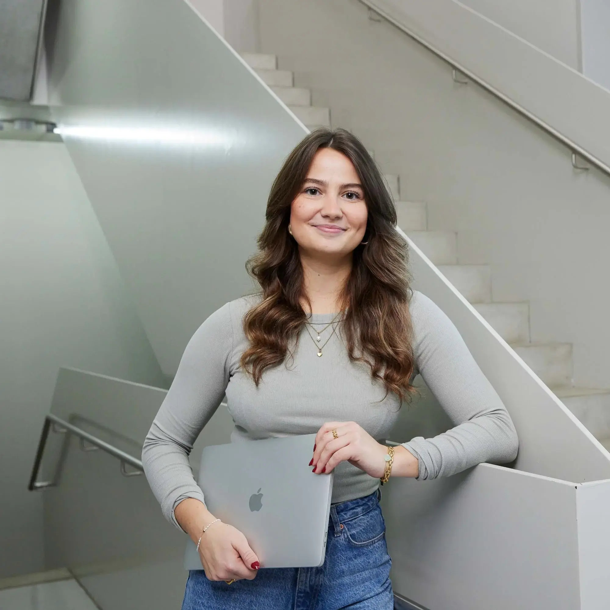 A student poses with her laptop on a staircase.