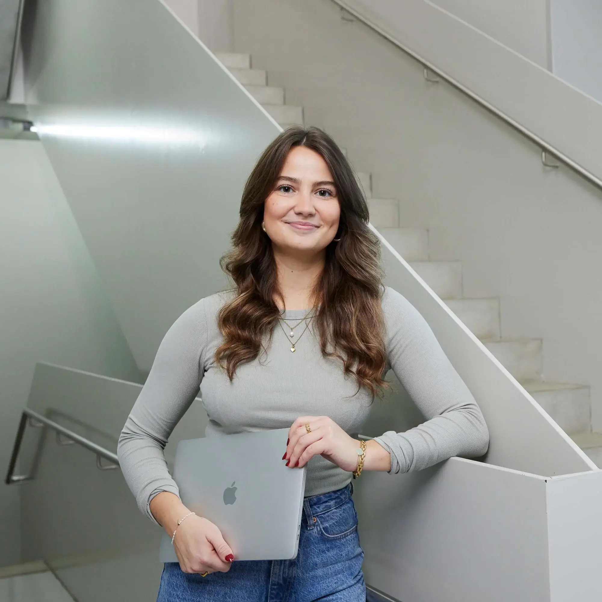 A student poses with her laptop on a staircase.