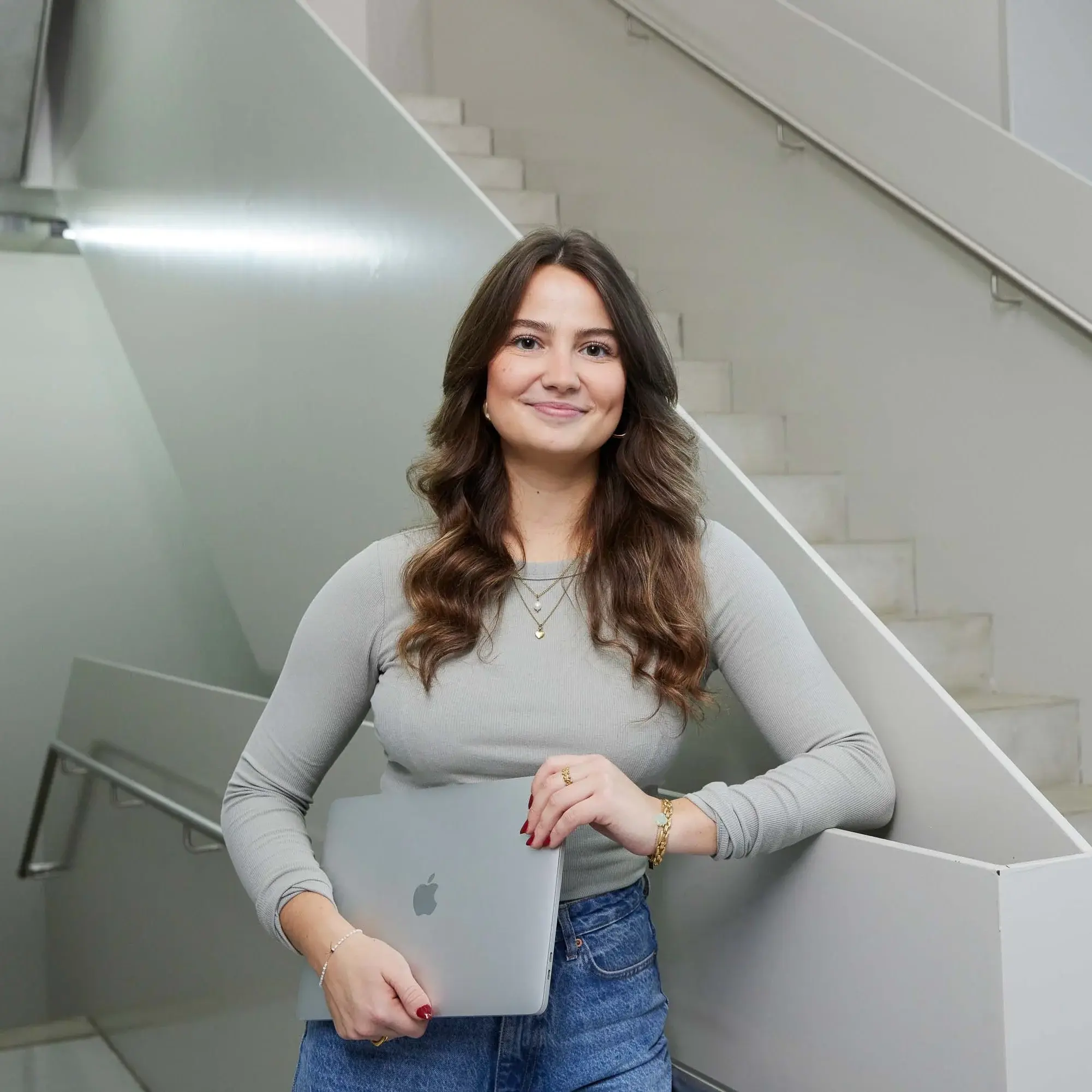 A student poses with her laptop on a staircase.
