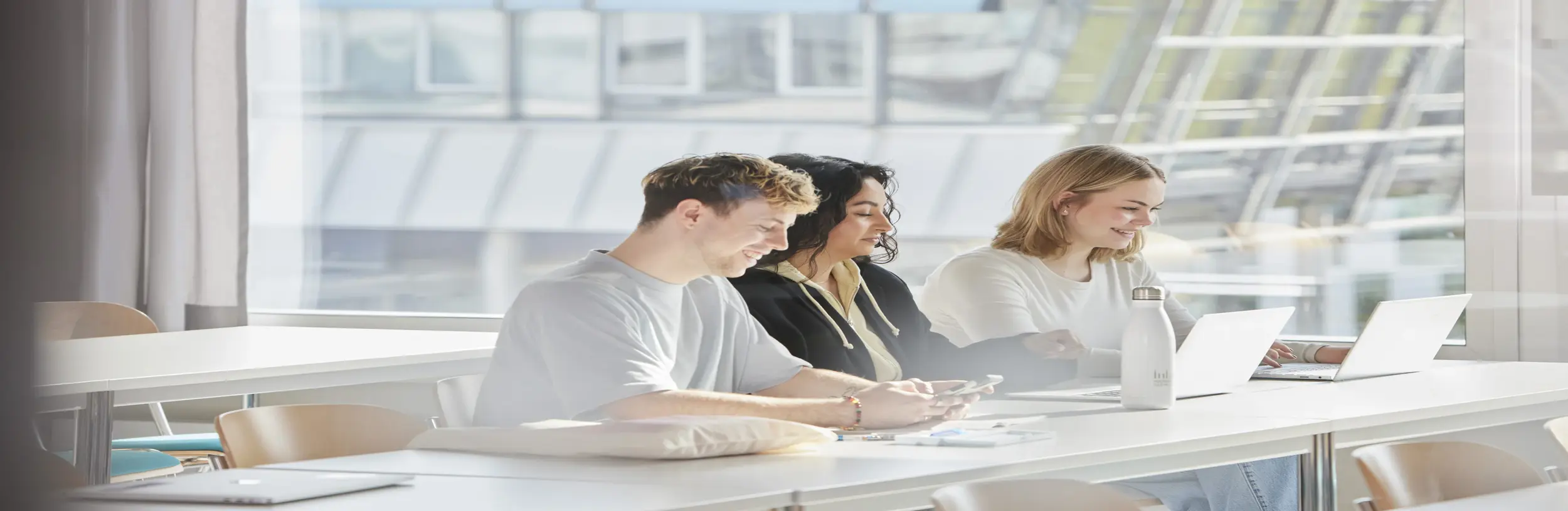 Drei Studierende sitzen in einem hellen Vorlesungsraum und arbeiten.