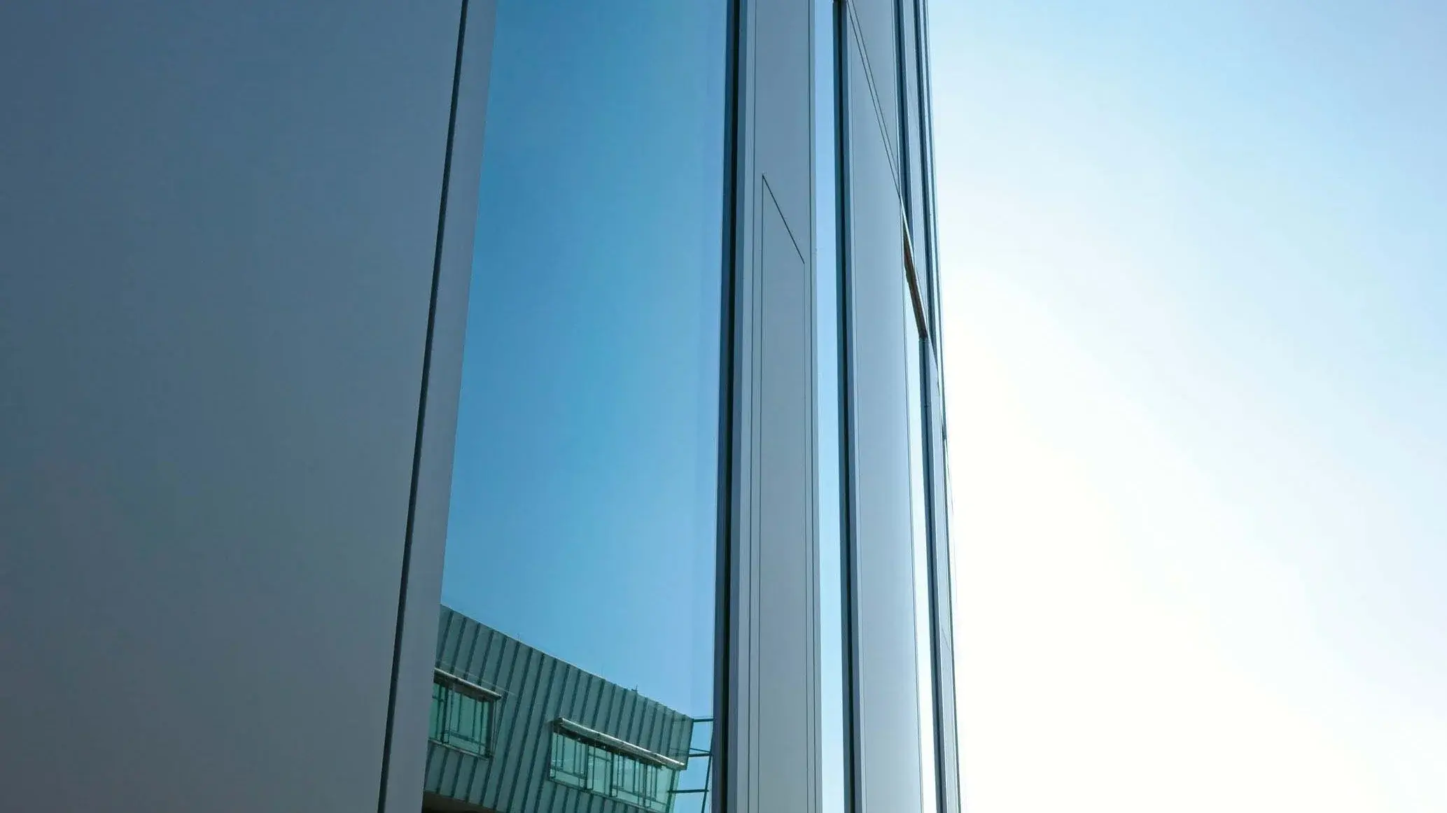 Nahaufnahme eines Hochschulgebäudes, in dessen Fenster sich das Hauptgebäude spiegelt.