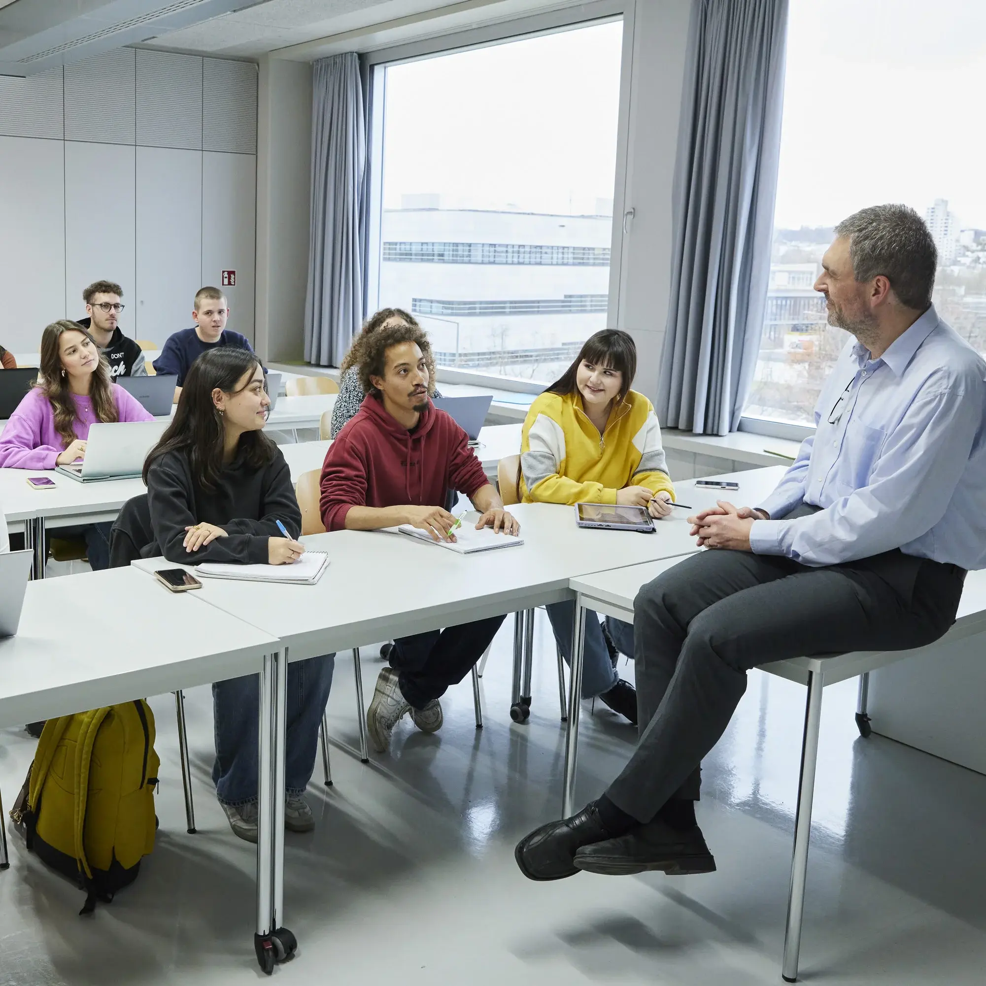 Professor sitzt auf seinem Tisch vor Studierenden in der Vorlesung.