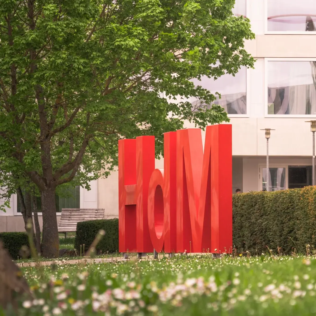 Logo der Hochschule der Medien auf einer Wiese vor einem Gebäude