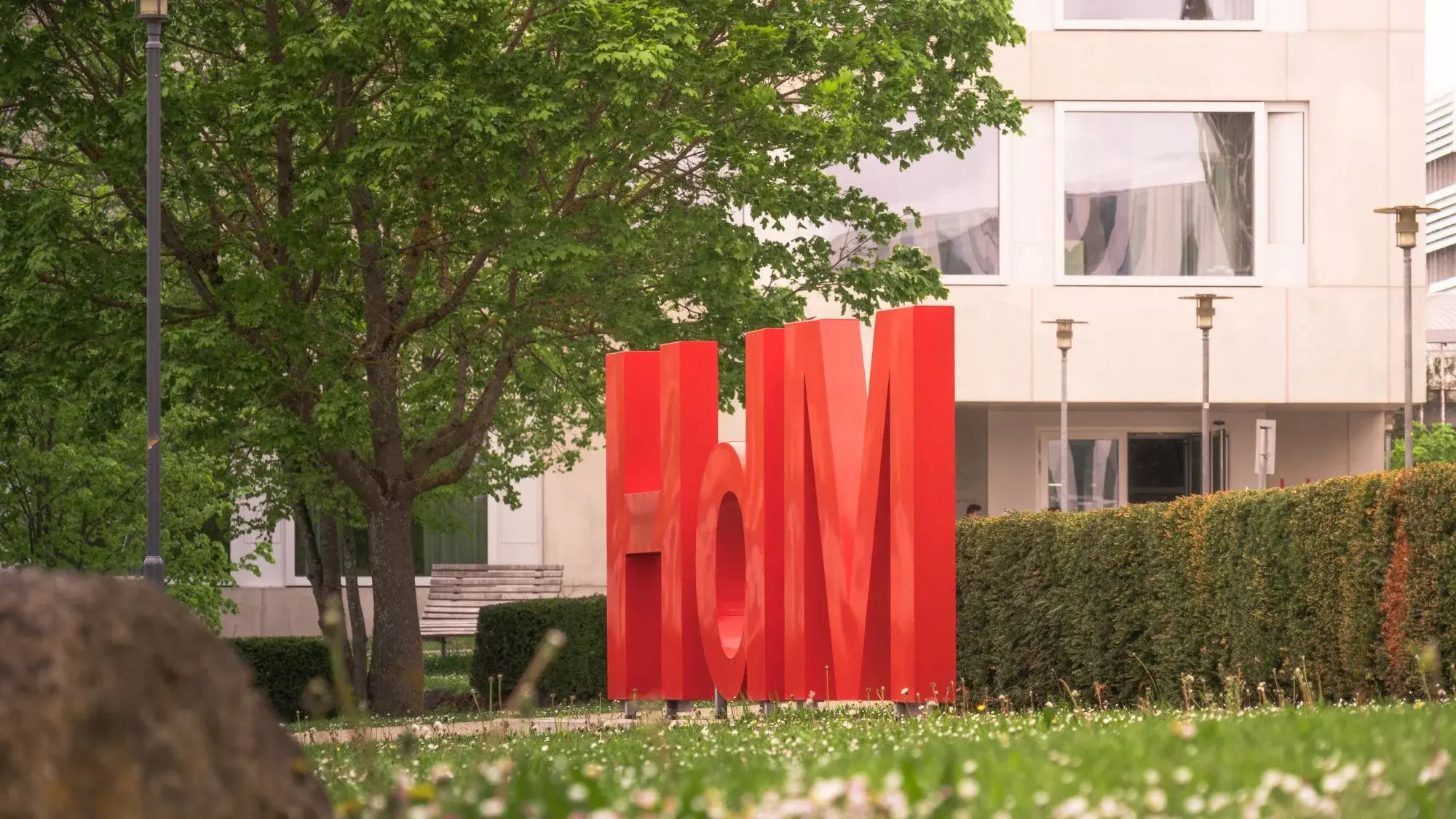 Logo der Hochschule der Medien auf einer Wiese vor einem Gebäude