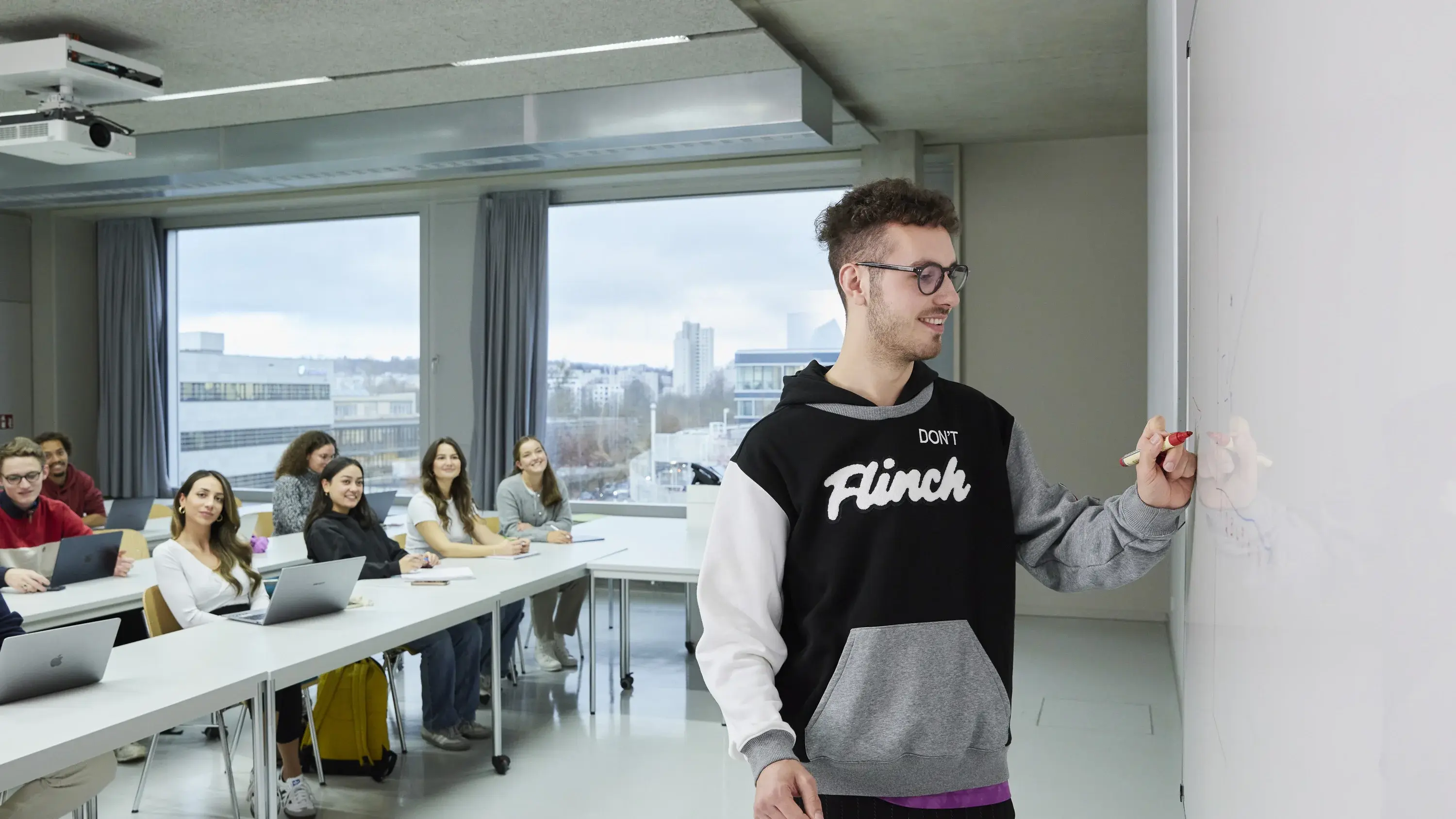 Ein Studierender zeichnet in einer Vorlesung mit einem Stift an die Tafel.
