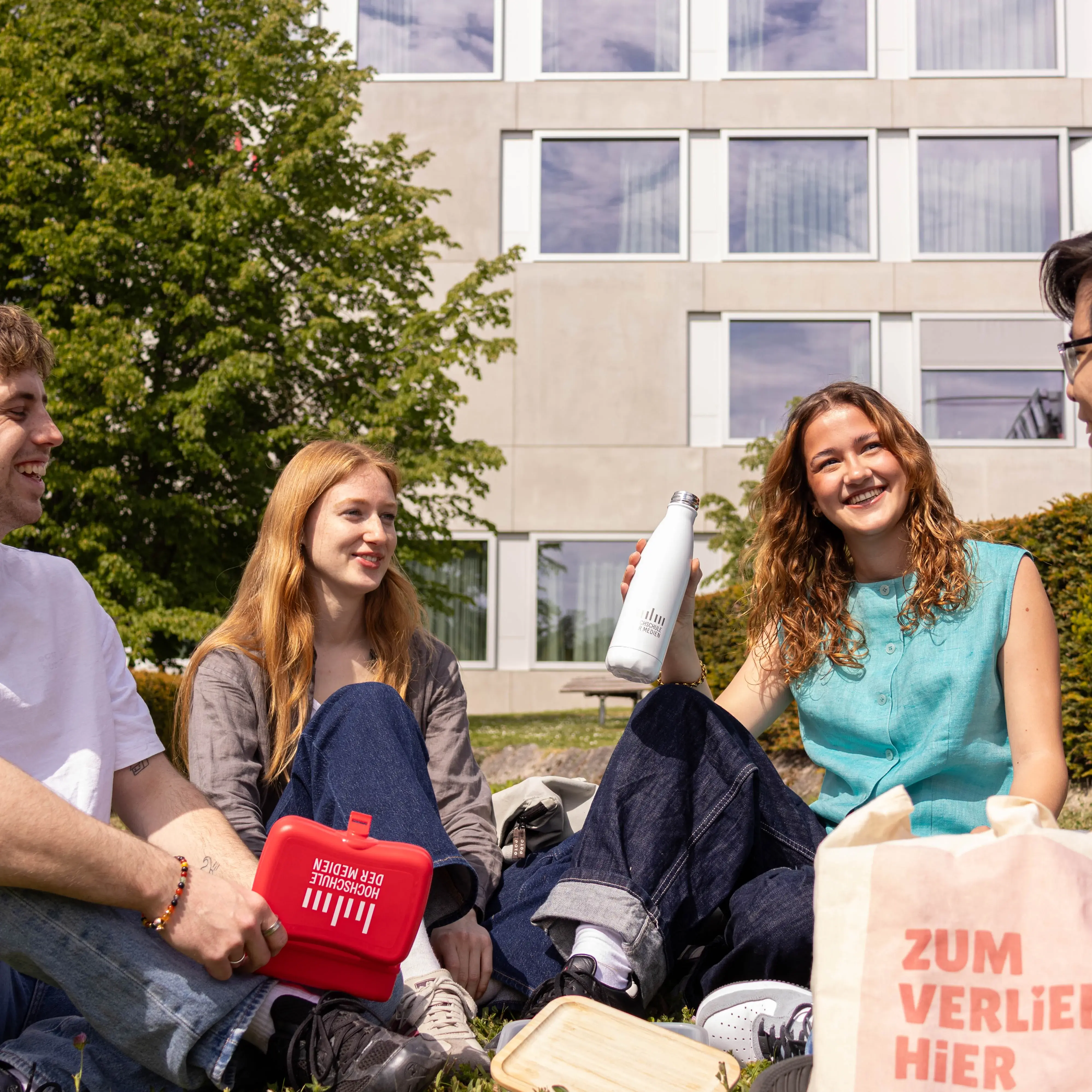Studierende verbringen ihre Pause auf der Wiese des sonnigen Campus der Hochschule der Medien.