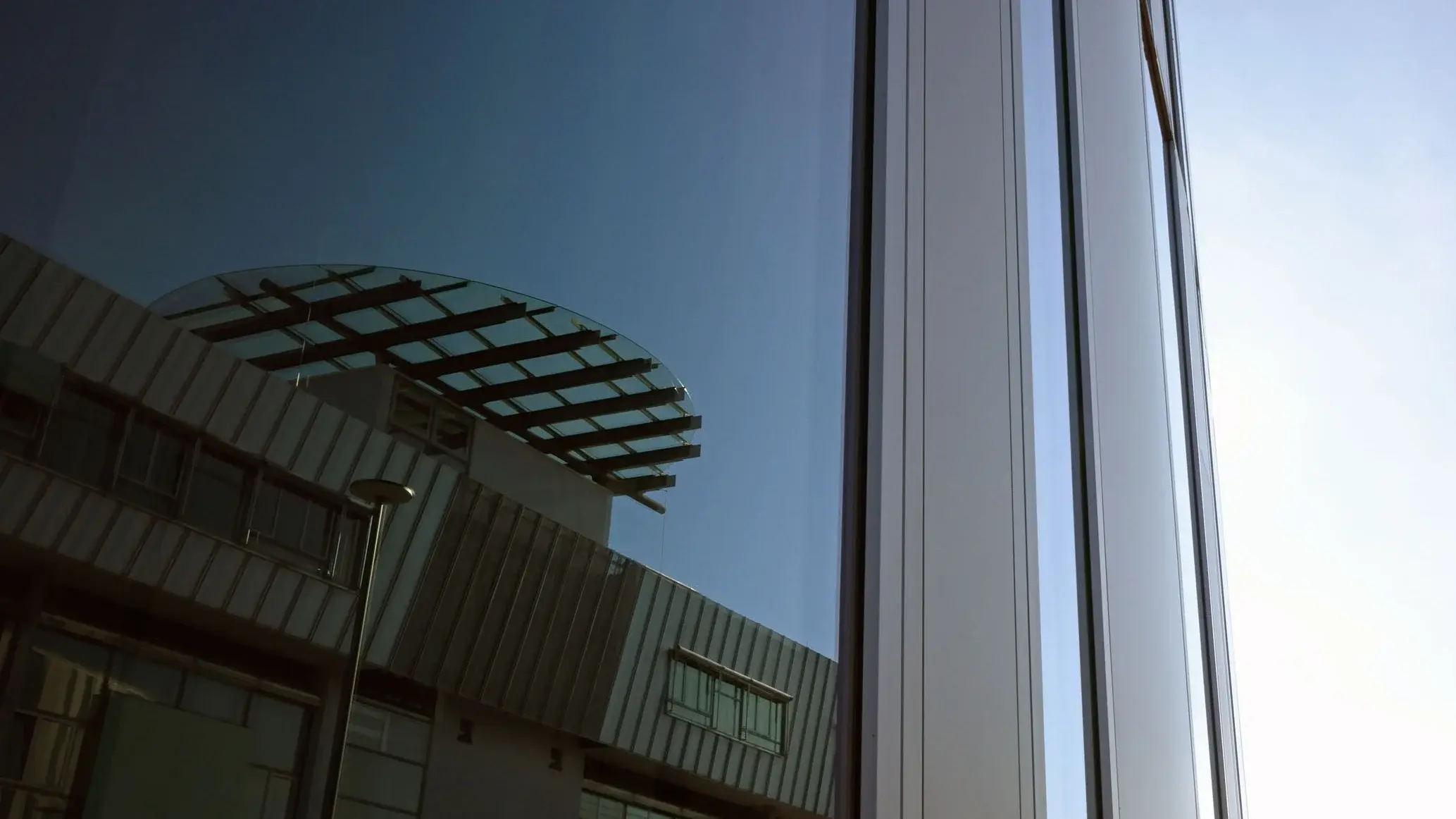Nahaufnahme eines Hochschulgebäudes, in dessen Fenster sich das Hauptgebäude spiegelt.
