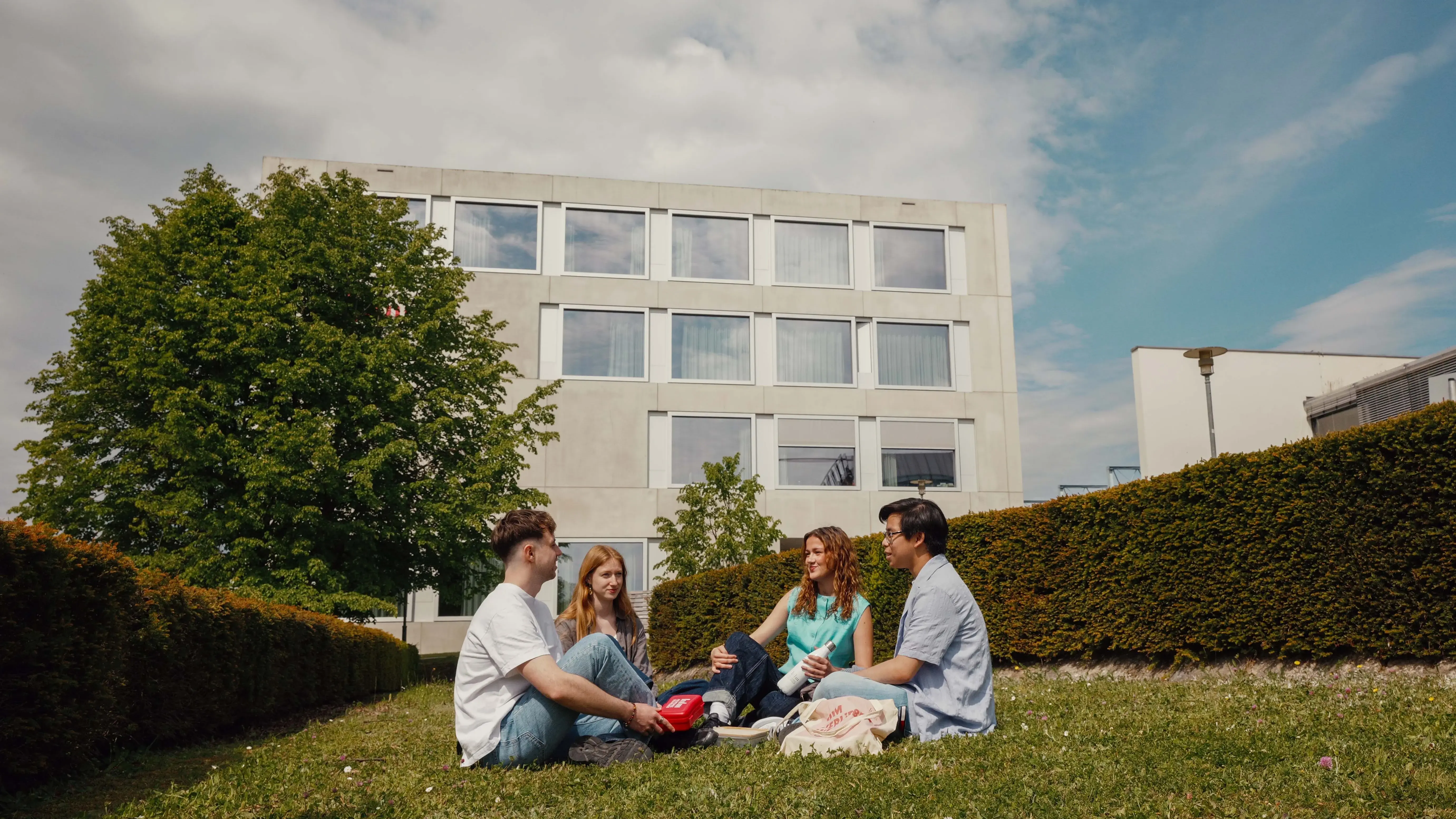 Studierende verbringen ihre Pause auf der Wiese des sonnigen Campus der Hochschule der Medien