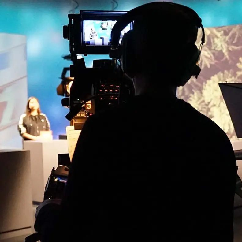 Ein Kameramann mit Kopfhörern filmt eine Moderatorin im Studio.