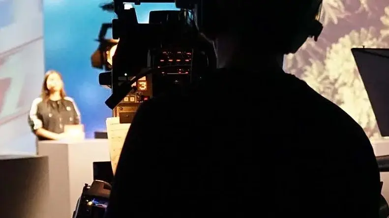Ein Kameramann mit Kopfhörern filmt eine Moderatorin im Studio.
