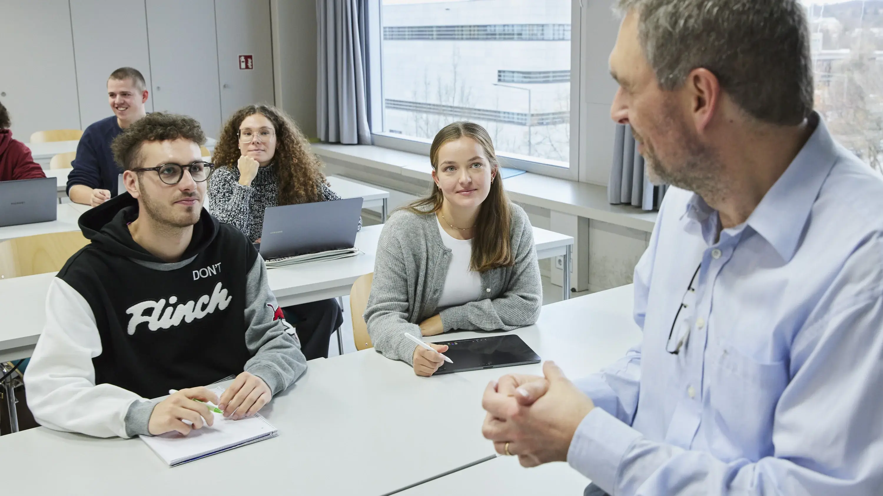 Ein Professor unterhält sich in einer Vorlesung mit einigen Studierenden.