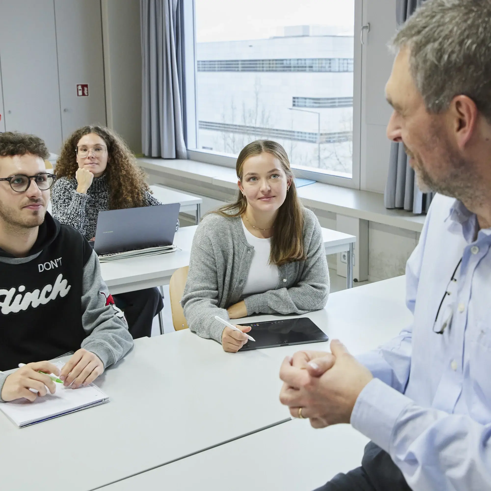 Ein Professor unterhält sich in einer Vorlesung mit einigen Studierenden.