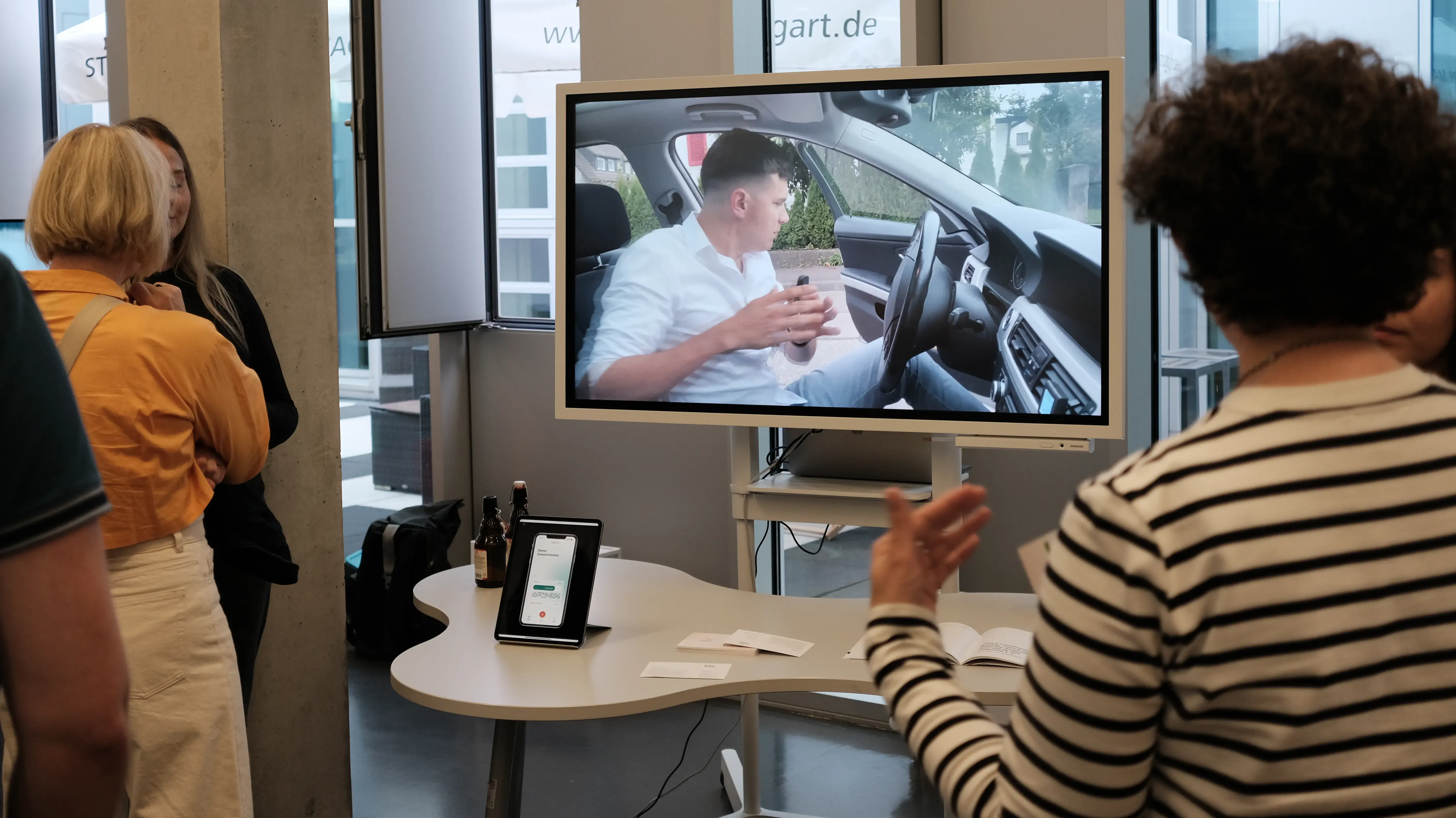 Studierende präsentieren ein interaktives Digital Design Projekt. Auf einem Monitor ist eine Videoszene aus dem Innenraum eines Autos zu sehen, die im Rahmen der Media Night erläutert wird.