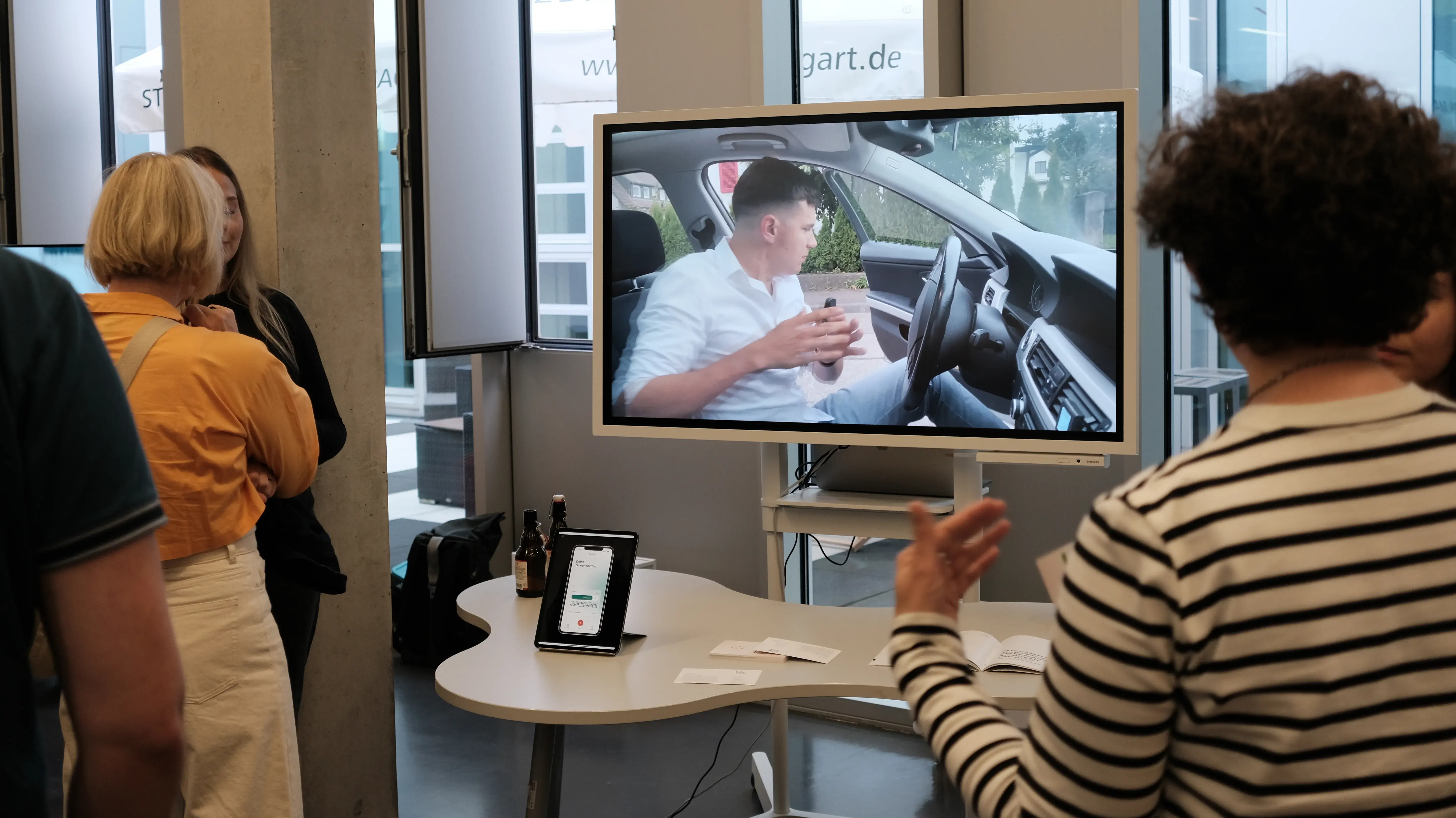 Studierende präsentieren ein interaktives Digital Design Projekt. Auf einem Monitor ist eine Videoszene aus dem Innenraum eines Autos zu sehen, die im Rahmen der Media Night erläutert wird.