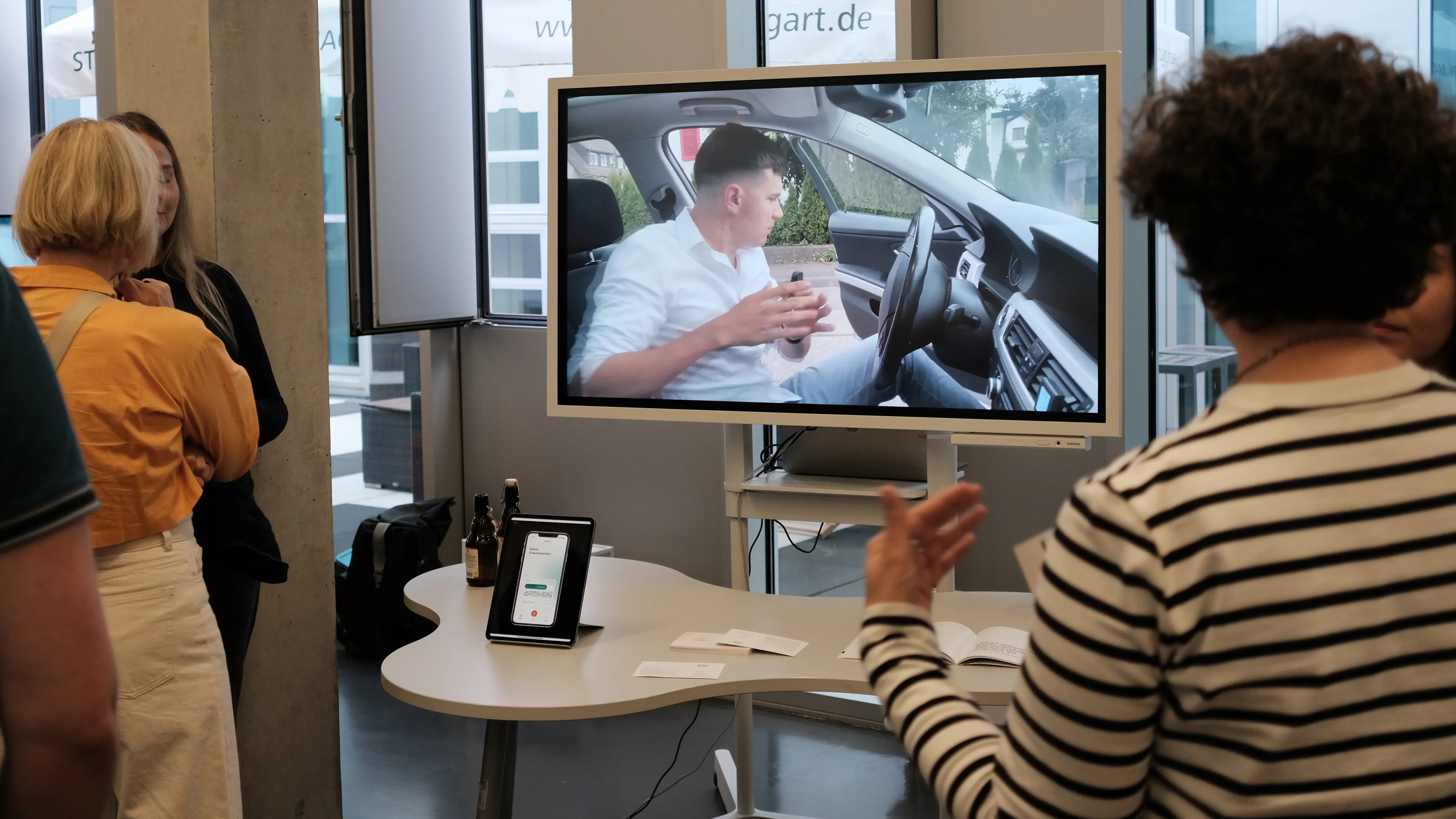 Studierende präsentieren ein interaktives Digital Design Projekt. Auf einem Monitor ist eine Videoszene aus dem Innenraum eines Autos zu sehen, die im Rahmen der Media Night erläutert wird.