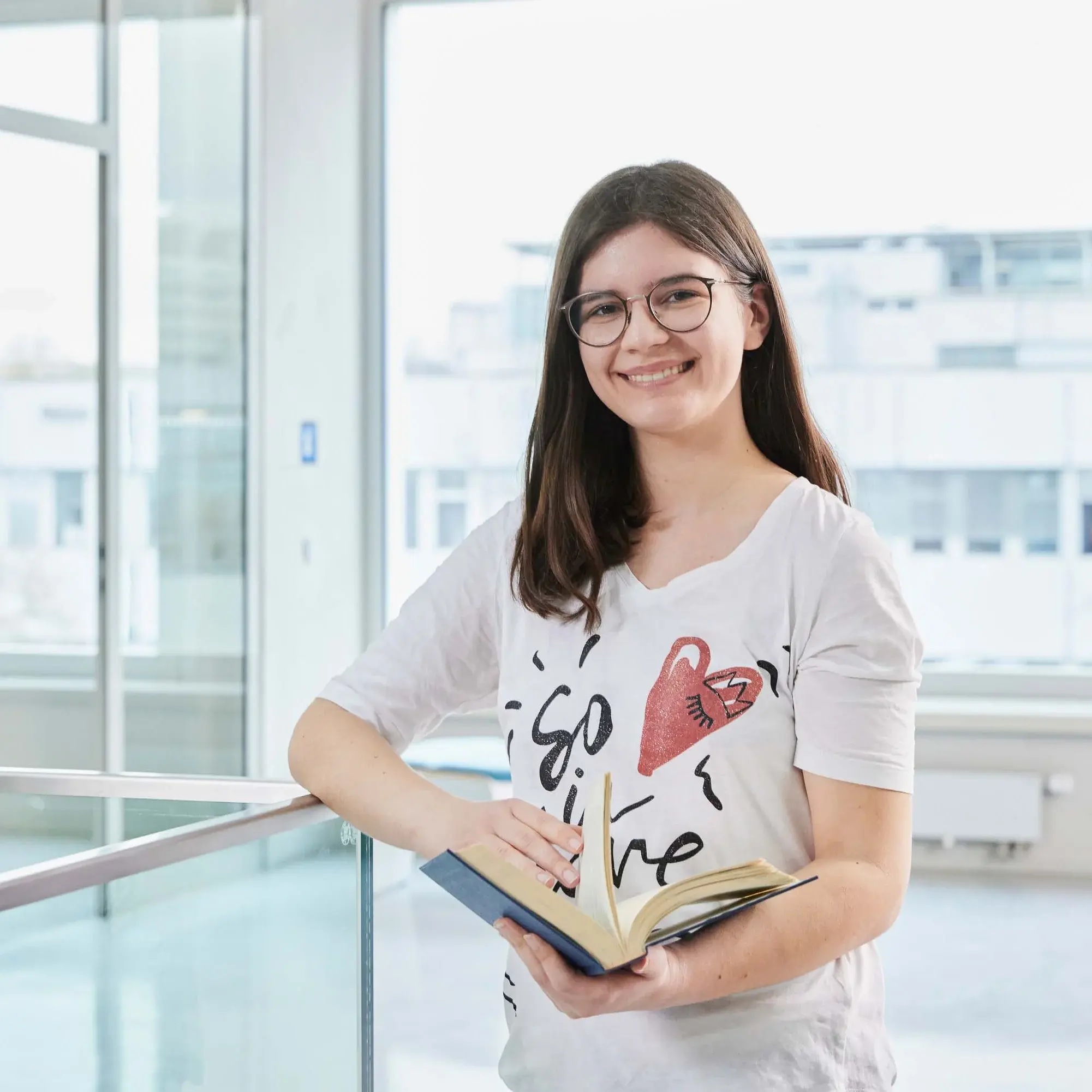 Eine Studierende steht mit ihrem Buch auf dem Gang der Hochschule der Medien.