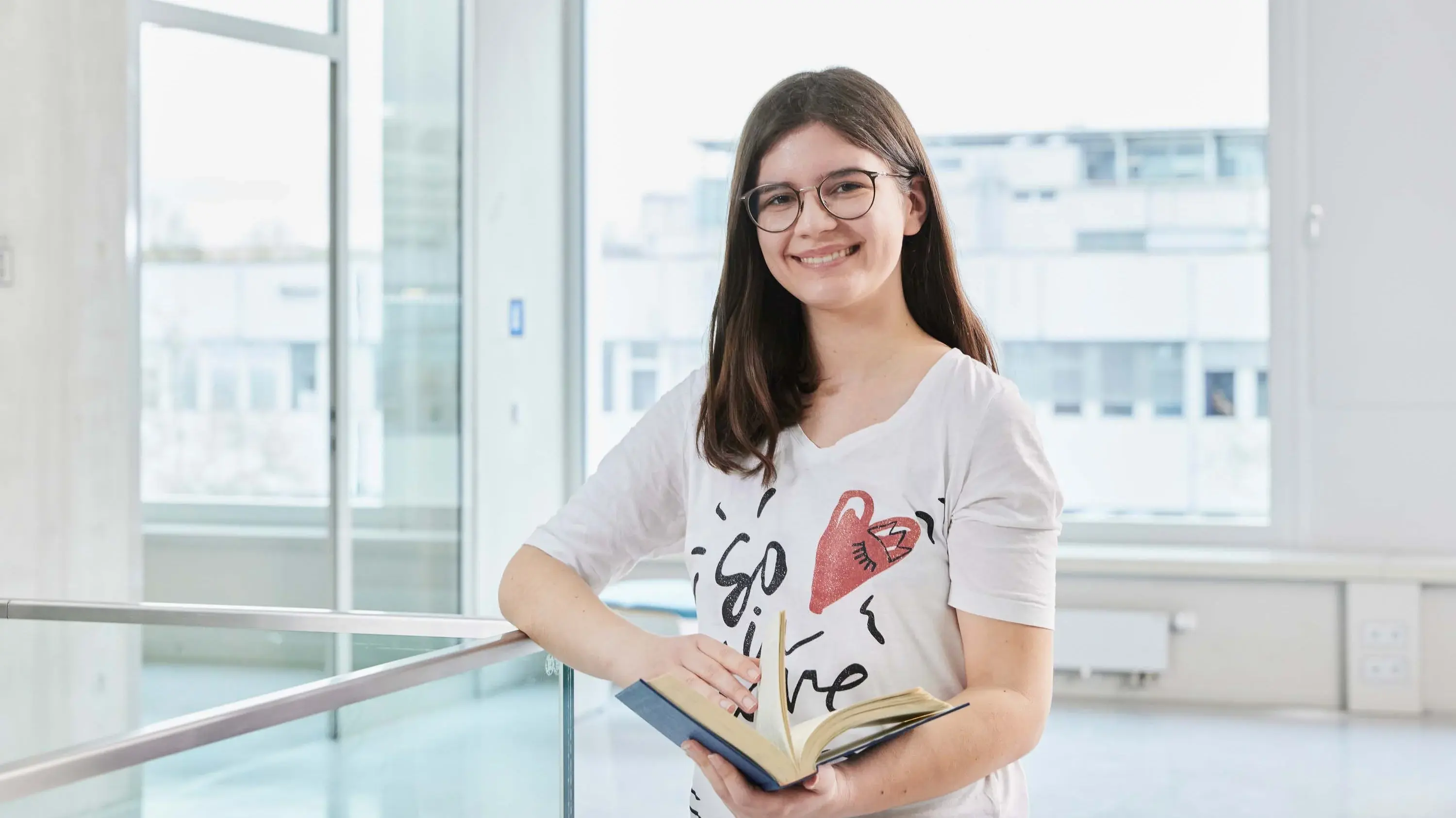 Eine Studierende steht mit ihrem Buch auf dem Gang der Hochschule der Medien.