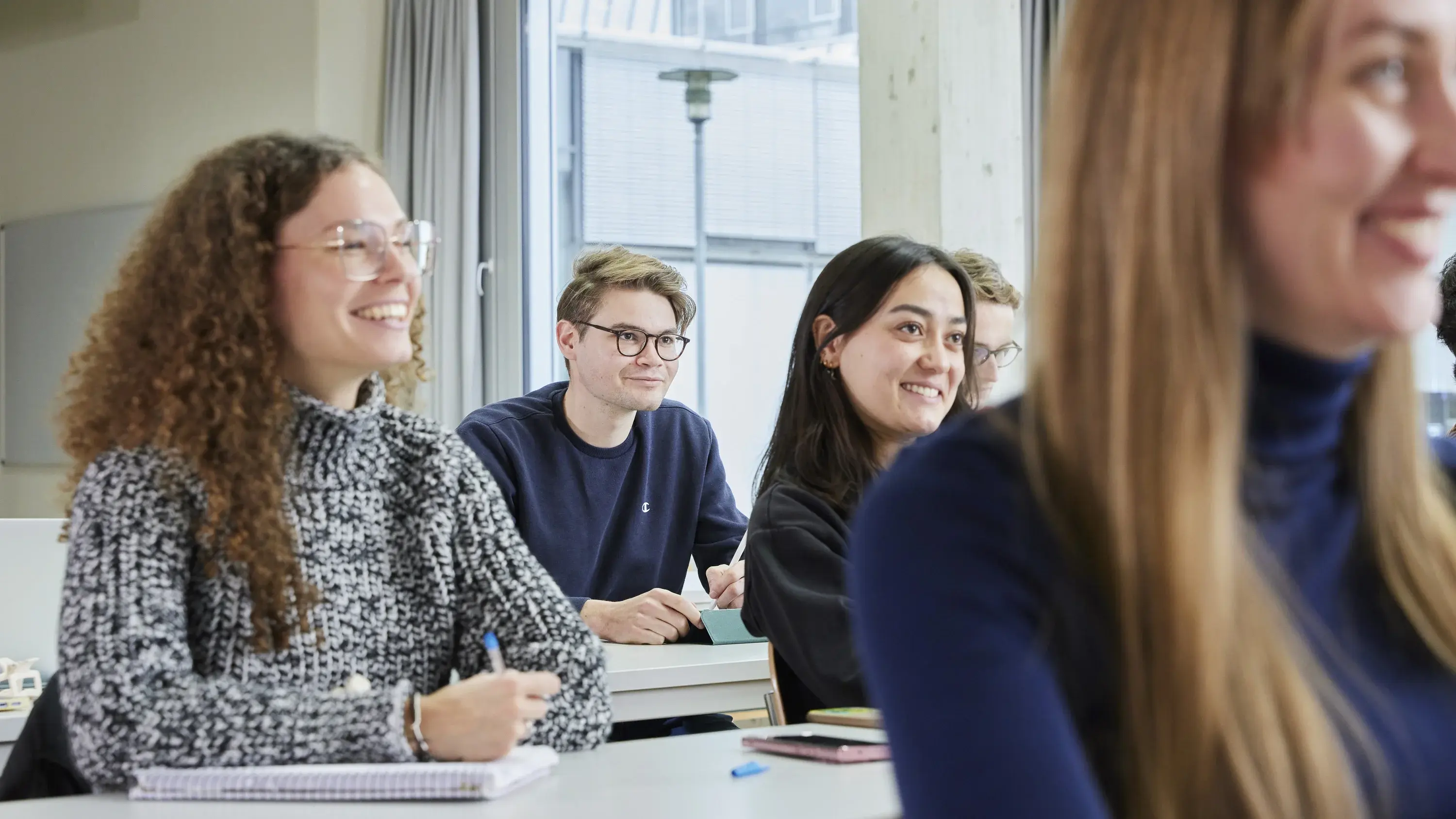 Studierende sitzen lachend in einer Vorlesung.