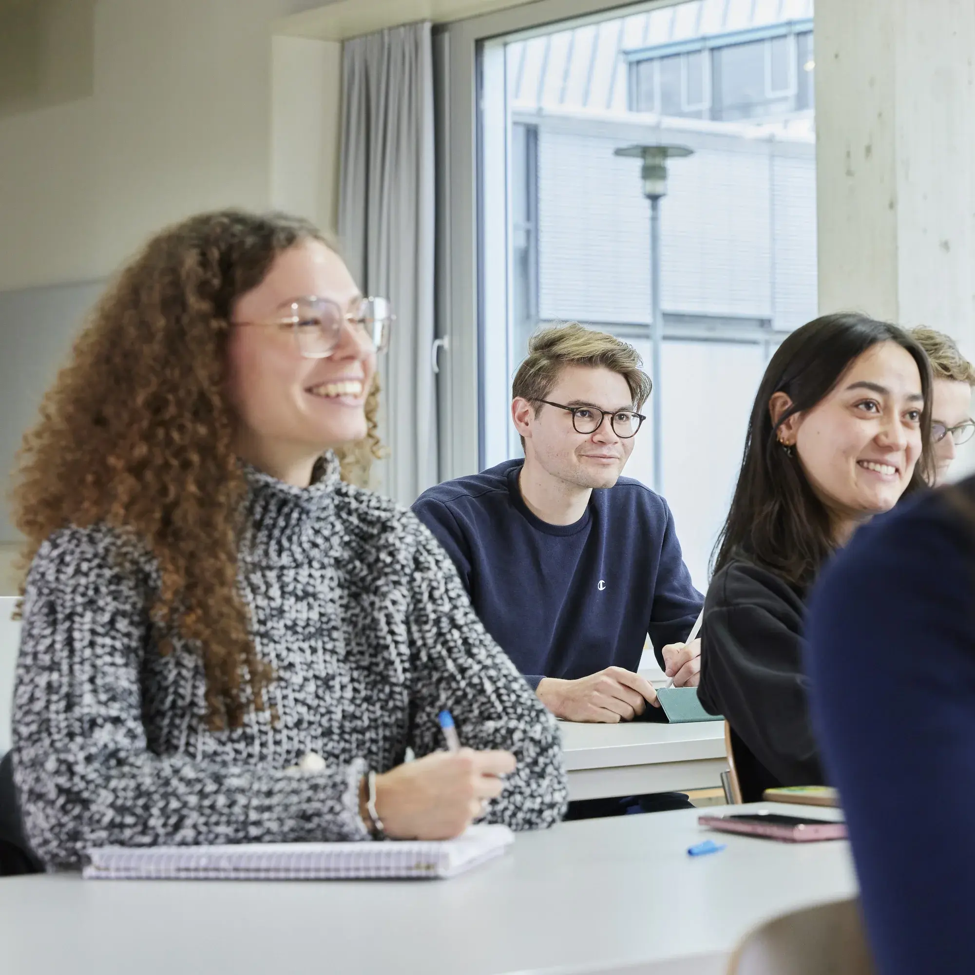 Studierende sitzen lachend in einer Vorlesung.